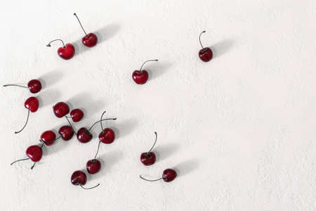 Scattering of ripe cherry berries on white table. Top view, long shadows, copy space.の写真素材