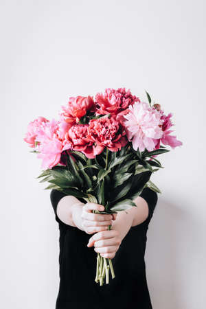Faceless girl holds a bouquet of peonies on concrete wall background. Incognito flower delivery....