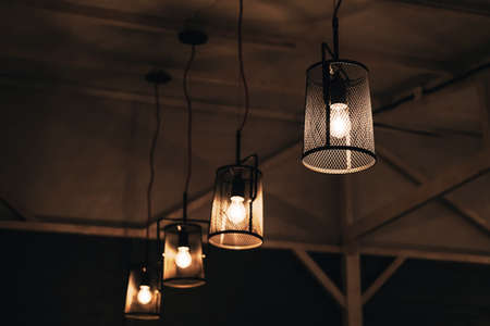 Group of lamps in mesh metal shades against the background of rough wooden ceiling. Blurred loft...