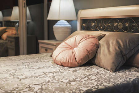 Classic style bed with velvet pillows on floral design bedspread. Fragment of bedroom interior in classic style, evening lightingの写真素材