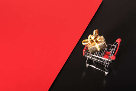 Golden gift box and shopping cart on black red background. Black friday sale.