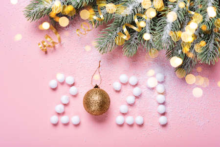 Figures 2021 made from snowballs and a Christmas ball on pink background, spruce branches and golden...