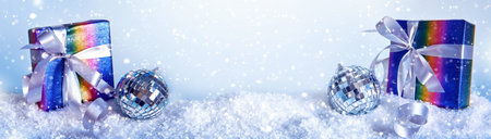 Blue Christmas banner with rainbow colors gift box and disco ball in snowdrift, copy space