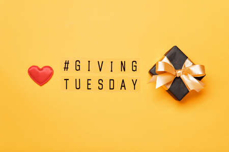Giving Tuesday text message. Global day of charitable giving after Black Friday shopping day. Red heart and gift on yellow backgroundの写真素材