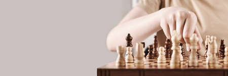 Banner with Faceless boy develops game strategy. Hand holds chess piece and makes a move, selective focus on handの写真素材