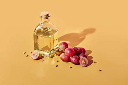 Grape seed oil in bottle and bunch of grapes on yellow background and trendy shadows. Reuse food wasteの写真素材