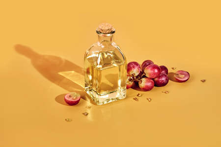 Grape seed oil in bottle and bunch of grapes on yellow background and trendy shadows. Reuse food wasteの写真素材