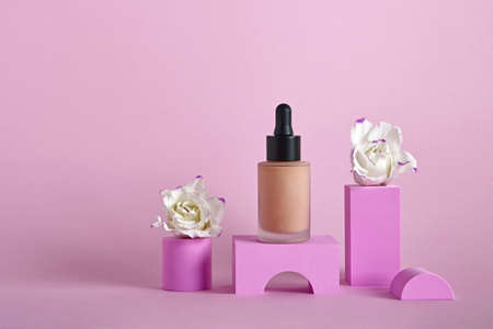 Liquid makeup foundation in bottle and flowers on different geometric podiums.の写真素材