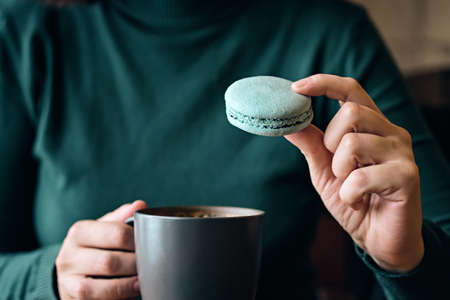 Woman faceless with coffee cup and macaroon sits at cafe table close-up. Selective focusの写真素材