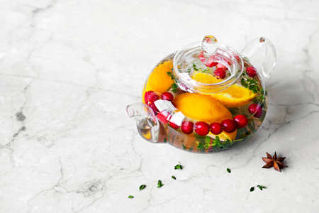 Immunity boosting drink. Thyme Tea with cranberries, orange and spices in glass teapot on marble tableの写真素材