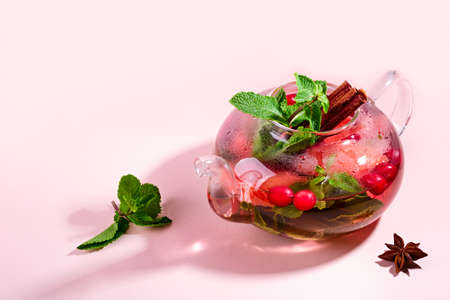 Immunity boosting drink. Mint Tea with cranberries, grapefruit and spices in glass teapot on pink table, trendy shadowsの写真素材