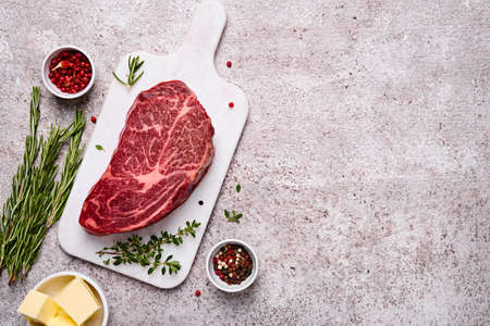 Fresh marbled beef rib eye steak, butter and spices on grey stone background, copy spaceの写真素材