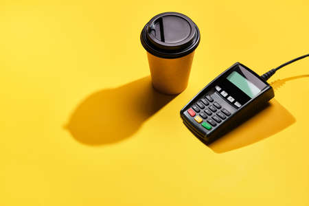 POS payment terminal and coffee on yellow background. Minimal financial service concept. Trendy...