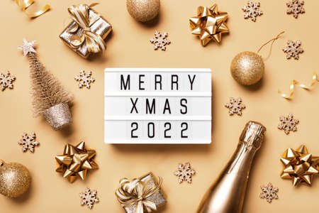 Lightbox with text MERRY XMAS 2022 and golden christmas decor on beige background. Creative layout in neutral monochrome colorsの写真素材