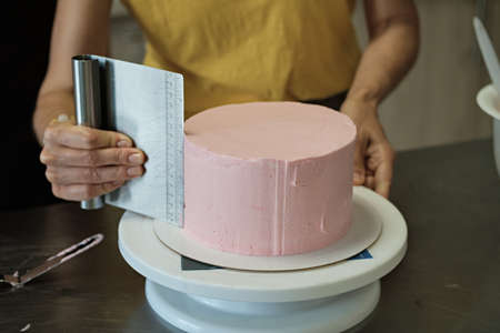 Woman spreads pink cream on cake, close-up. Cake making process, Selective focus