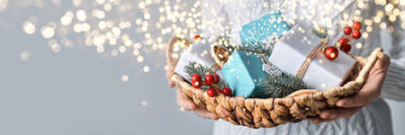Woman holding basket with sustainable wrapped Christmas gifts, close-up, selective focus. Eco Christmas decor, banner formatの写真素材