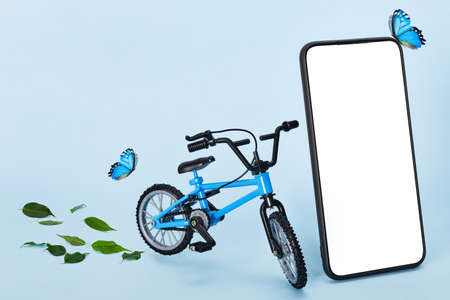 Creative eco delivery concept. Smartphone with copy space, Bicycle and butterflies on blue...