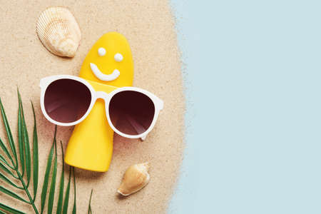 Yellow tube with happy sunscreen face and sunglasses. Sun Ultraviolet protection cosmetics product creative concept.の写真素材