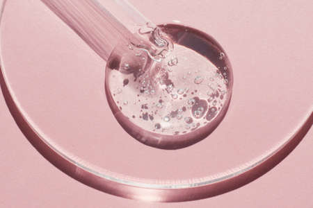 Pipette with sample of gels cosmetic product in petri dish on pink background, hard shadowsの写真素材