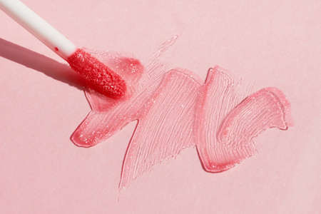 Smears of shining lip gloss and lip gloss brush on pink background, hard shadowsの写真素材