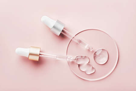 Two pipettes with different samples of gels cosmetic products in petri dish on pink backgroundの写真素材