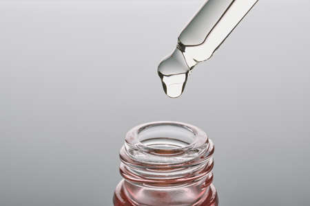Oil or Serum bottle and pipette close-up on grey background. Pink cosmetic product, selective focus