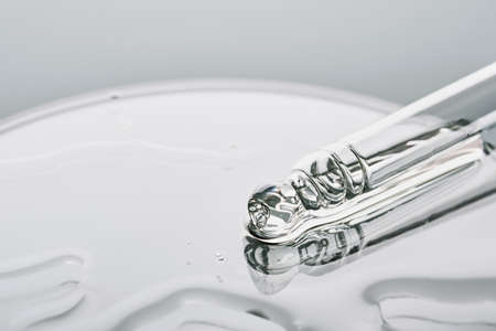 Pipette with sample of cosmetic product in petri dish on grey background, selective focusの写真素材