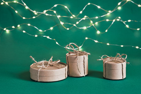 Christmas sustainable round gift boxes and shining garland on green background. Christmas zero waste