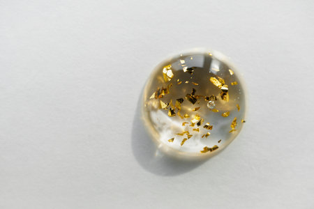 Serum drop with gold particles close-up, copy space. Beauty skin care product swatch.