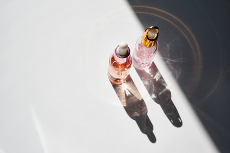 Cosmetic product bottles with rose petals and hard shadow. Skincare beauty product conceptの写真素材