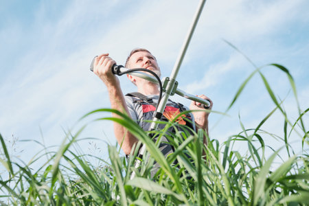 Man in overalls with weed trimmer mowing tall grass on sky backgroundの写真素材