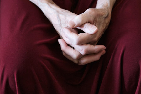 Elderly caucasian female hands resting on burgundy fabricの写真素材