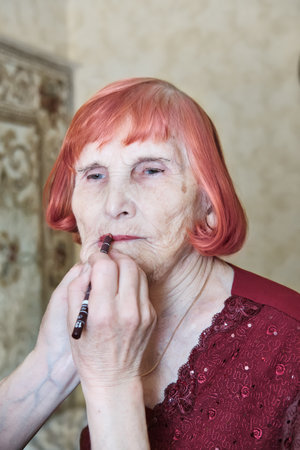 Elderly caucasian woman receiving makeup touch-up, red hair, ornate dressの写真素材