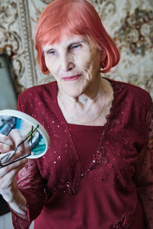 Elderly caucasian woman with red hair admires his reflection in mirror indoors