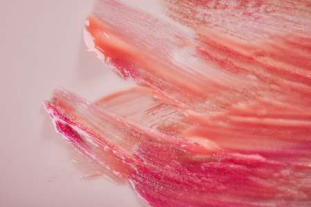 Pink and coral lip gloss smears on pink pastel background close-up