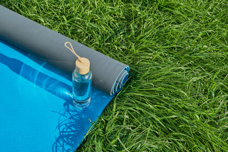 Yoga mat and water bottle on green grass for outdoor fitness and relaxation