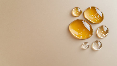 Honey-colored liquid droplets on beige surface with bubbles highlighting fluid textureの素材