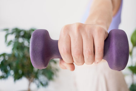Caucasian female exercising with purple dumbbell in hand close-up.