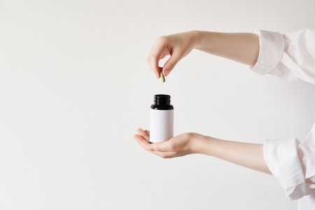 Female putting green capsule into blank medicine bottle on white backgroundの写真素材