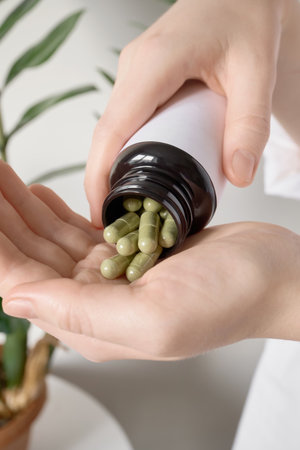 Female hands pouring green herbal capsules from bottle into palm showing wellness