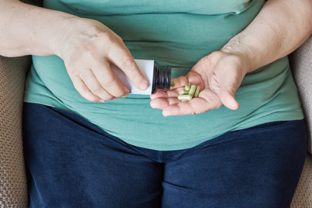 An overweight Mature woman pouring green capsules from a bottle into her hand for daily health and wellnessの写真素材