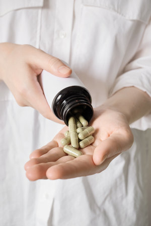 Person pouring dietary supplements or medicine into an open palmの写真素材