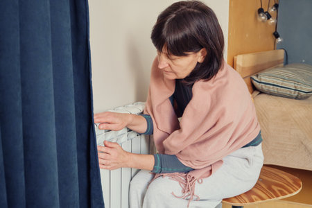 Woman feeling cold pressing hands against room radiator for warmthの写真素材