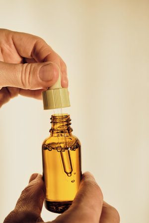 Hands holding an amber bottle with dropper full of essential oil, symbolizing natural skincare
