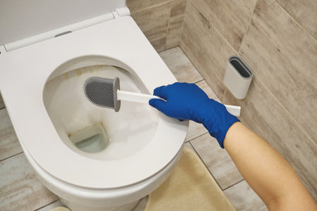 Hand in blue rubber glove cleaning filthy ceramic toilet bowl with modern silicone brushの写真素材