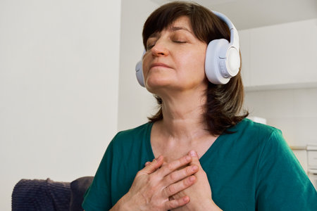 Woman wearing headphones with eyes closed embracing self-care and mindfulness at homeの写真素材