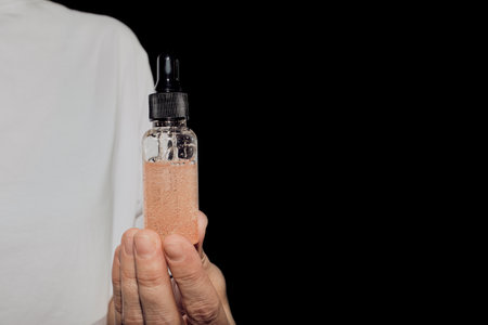 Hand holding glass dropper bottle containing skincare serum against black background