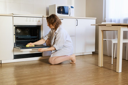 Woman cleaning oven door with sponge, completing household chores in kitchenの写真素材