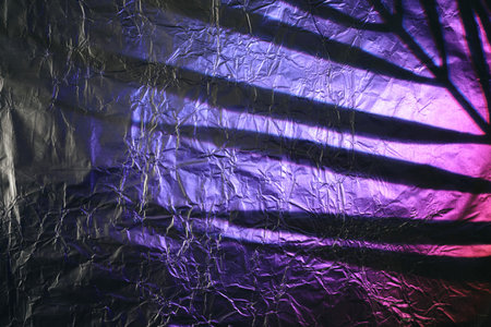 Crumpled aluminum foil surface displaying cast shadow with purple and pink light