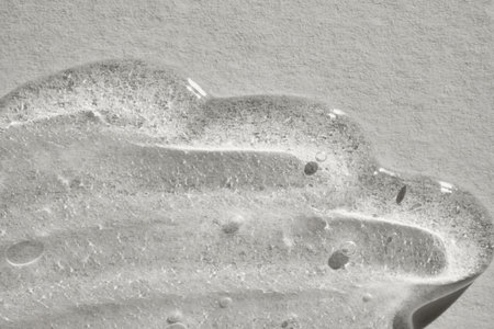 Transparent cosmetic gel with air bubbles creating textured pattern on neutral surface